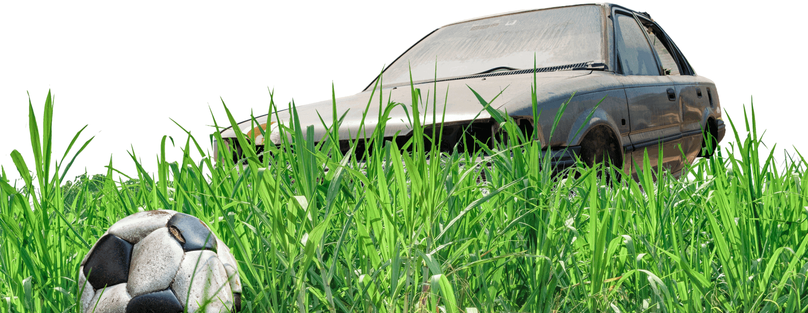 An image of a damaged soccer ball sitting in tall grass with an abandoned car in the background