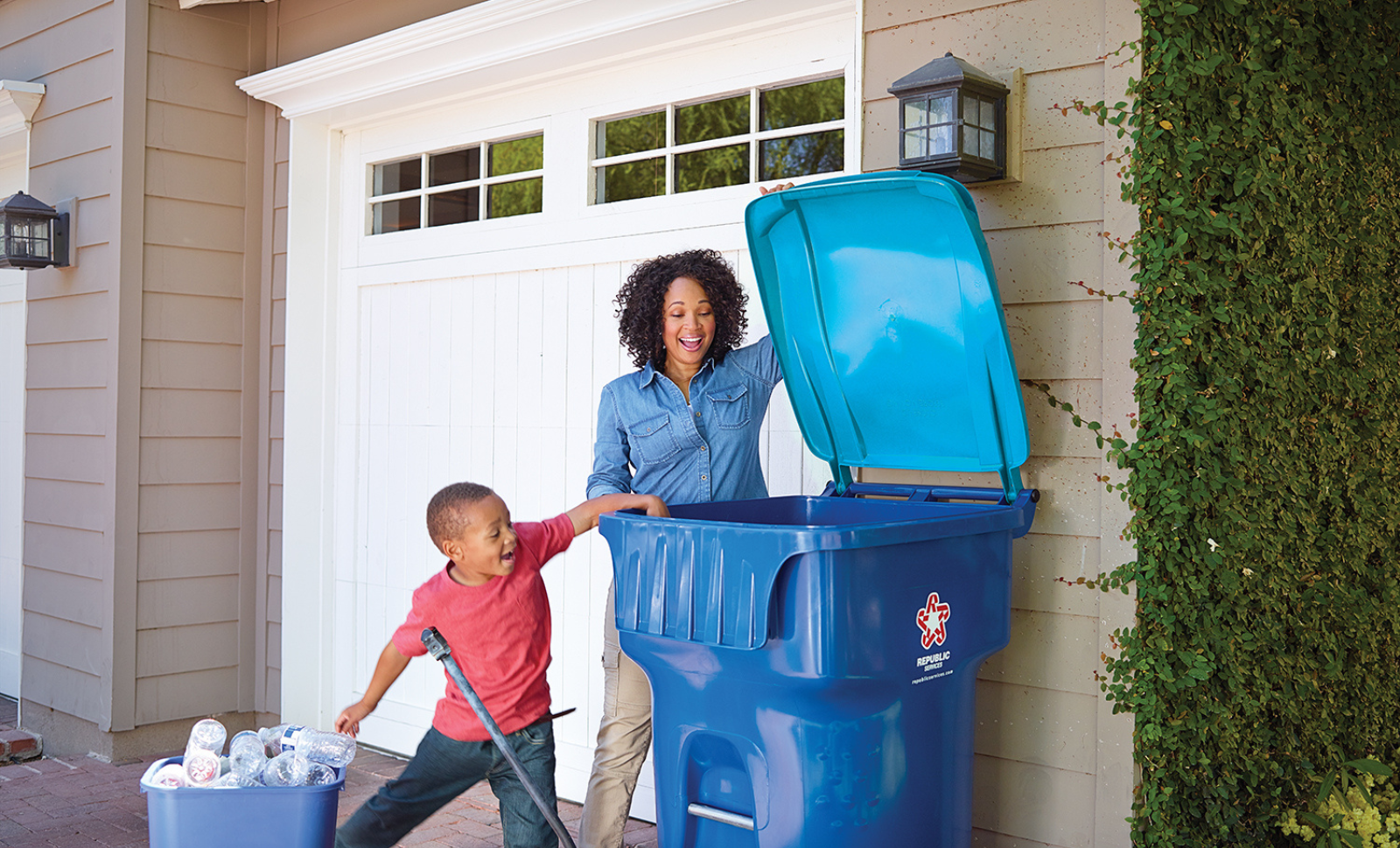 An image of a woman and a child placing an item inside a recycling cart
