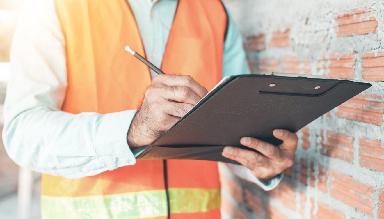 An image of someone wearing a reflective safety vest while holding a clipboard and pencil and making a mark on a piece of paper held on the clipboard