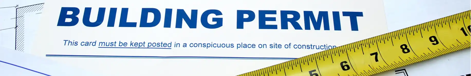 An image the words "Building Permit" across the top of a piece of paper, and a portion of a measuring tape laying on top of the paper