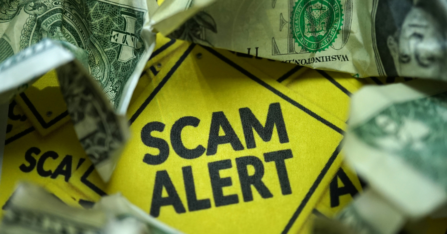 Image of "scam alert" warning sign surrounded by crumpled money