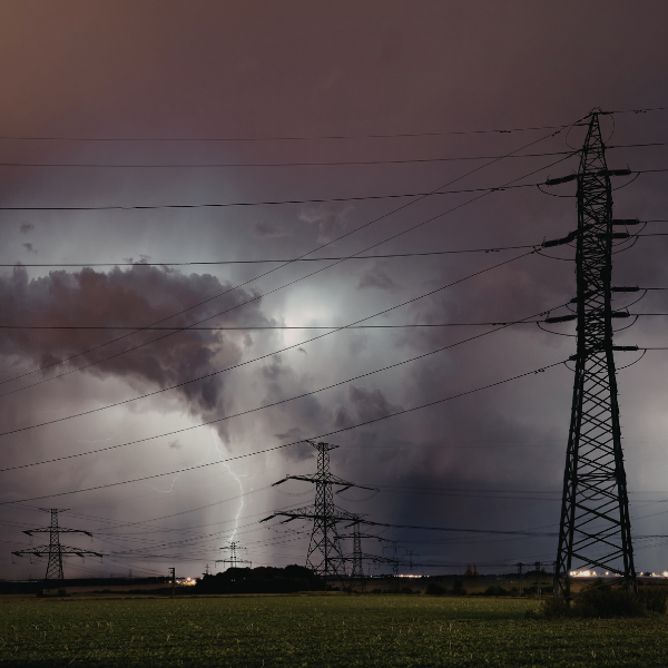 Image of a sky with dark clouds, rain and lightning, depicting a severe thunder storm. The image also depicts power transmission towers and power lines.