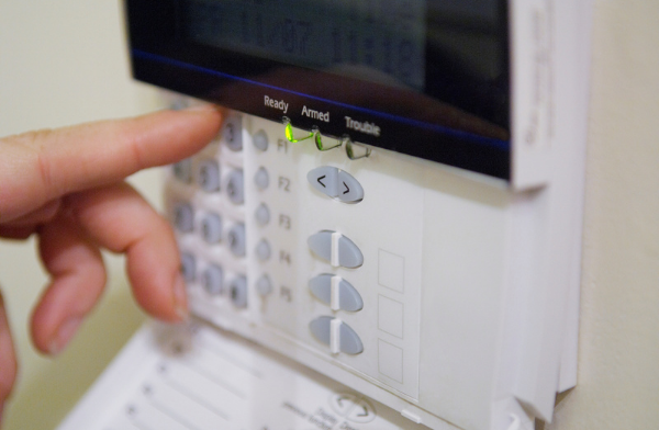 Image of a home security system keypad and someone touching the keypad to disarm or arm the system.